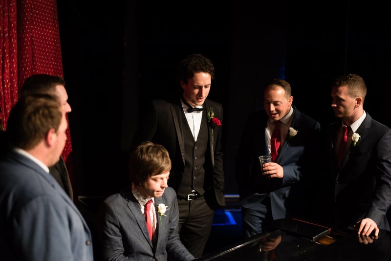 Bridebook.co.uk groom and party singing around piano
