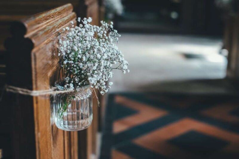 bridebook.com picture of a jar of baby's breath flowers tied to the side of a church pew