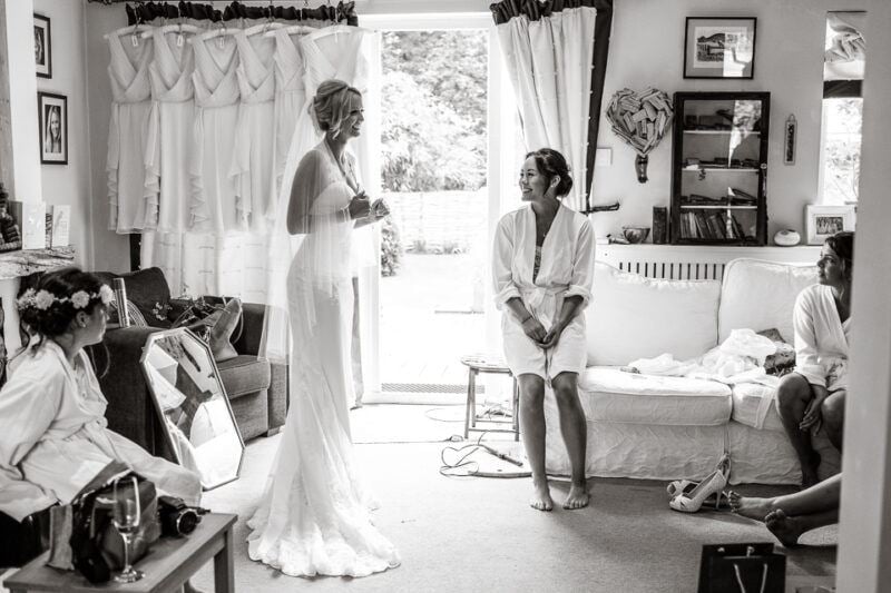 www.bridebook.co.uk bride in her dress as bridesmaid looks on smiling