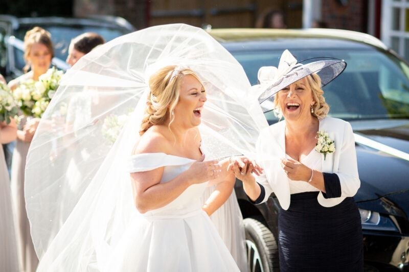 A bride and the mother of the bride laughing as they walk out of the car