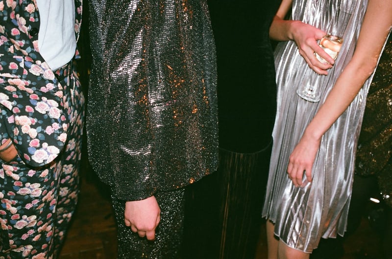 Gros plan sur des invités en tenues de soirée scintillantes et originales, avec une robe métallisée, un costume à motif floral et une coupe de champagne en main.