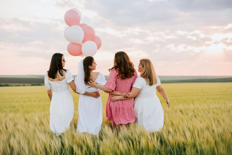 bride and three bridesmaids walking through a field holding balloons