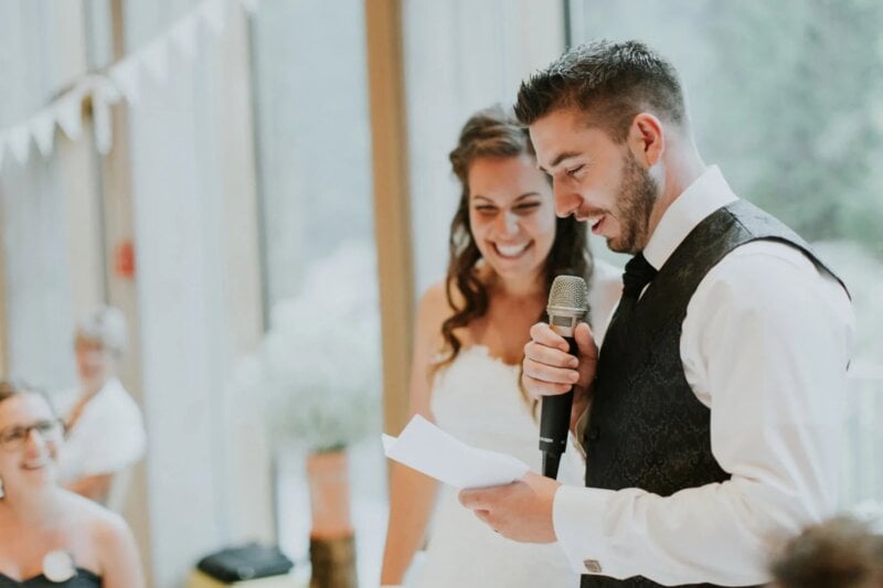 Bräutigam liest Glückwünsche zur Hochzeit vor, lächelnde Braut steht daneben