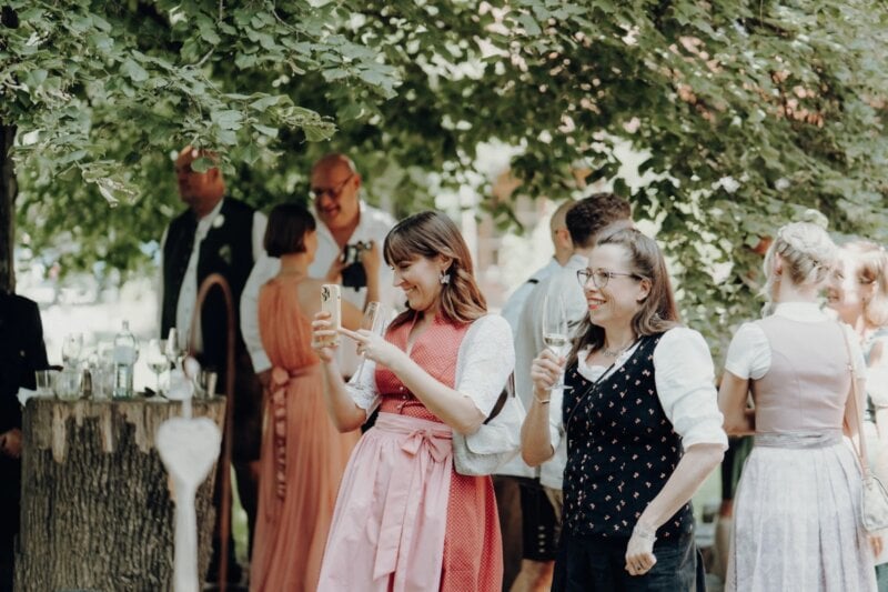 Hochzeitsgäste in Tracht filmen mit dem Handy und stoßen mit Sekt an