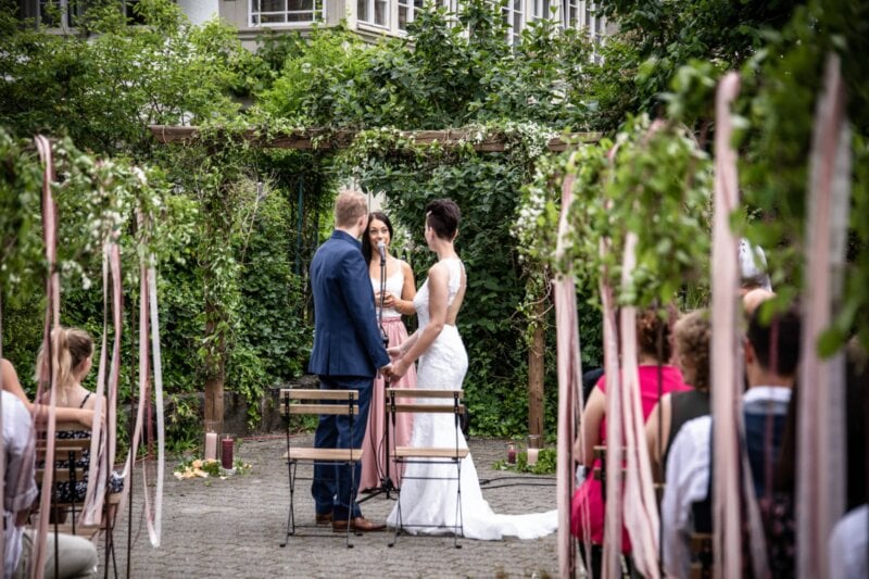 Trauzeugin hält Hochzeitsrede am Mikrofon zwischen Brautpaar im grünen Garten