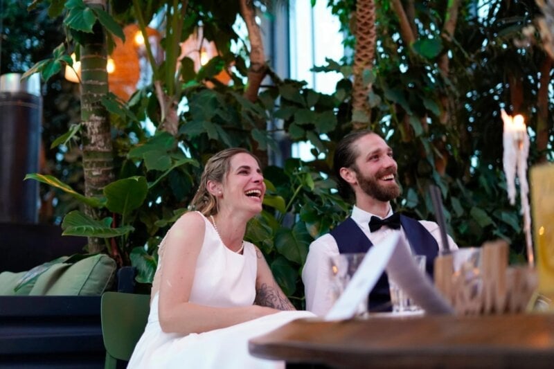 Brautpaar lacht herzlich am Tisch beim Zuhören der Glückwünsche zur Hochzeit