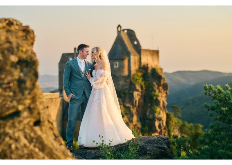 Brautpaar steht sich vor einer Burgruine bei Sonnenuntergang auf einem Felsen gegenüber