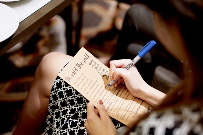 Hochzeitsgast füllt eine „He said She said“-Spielkarte mit einem Stift aus
