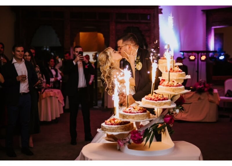 Brautpaar küsst sich vor mehrstöckiger Hochzeitstorte mit funkelnden Wunderkerzen