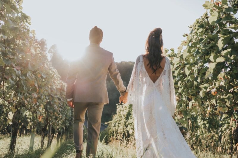 Brautpaar geht Hand in Hand durch die Weinreben im goldenen Abendlicht