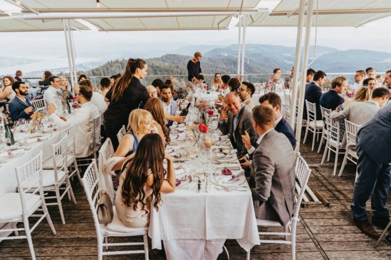 Hochzeitsgesellschaft speist auf überdachter Terrasse mit Panoramablick auf Berge und See