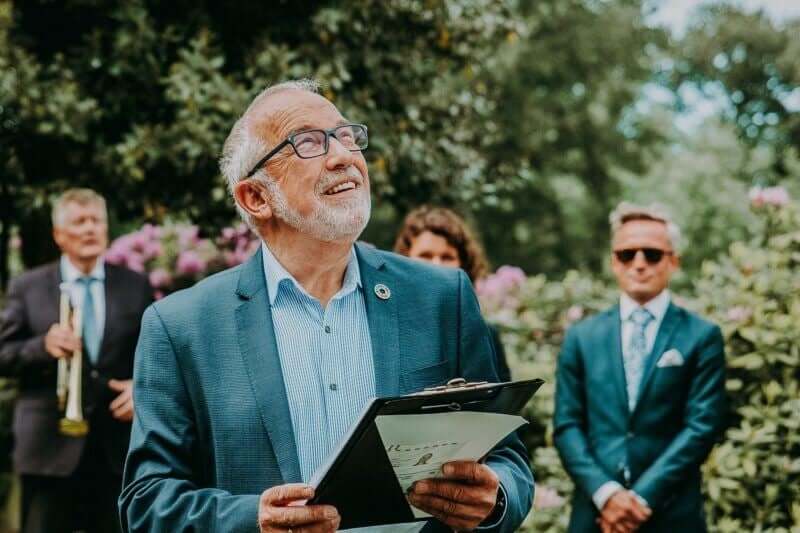 Vater des Bräutigams hält lächelnd Hochzeitsrede mit Redemappe im Garten