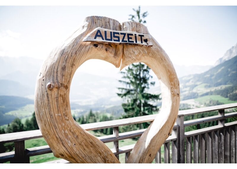 Herzförmige Holzskulptur mit Schild „Auszeit“ vor Bergpanorama – Symbol für eine gemeinsame Auszeit als Hochzeitsgeschenk