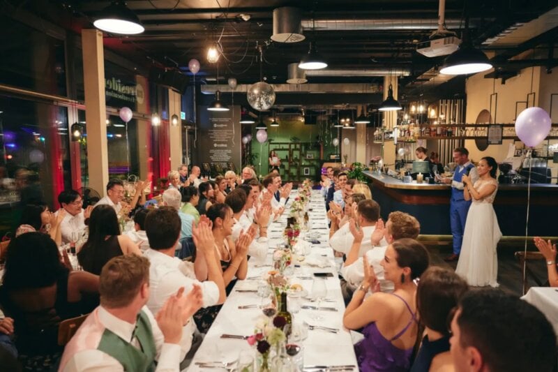 Applaudierende Hochzeitsgäste an festlich gedeckter Tafel feiern mit dem Brautpaar