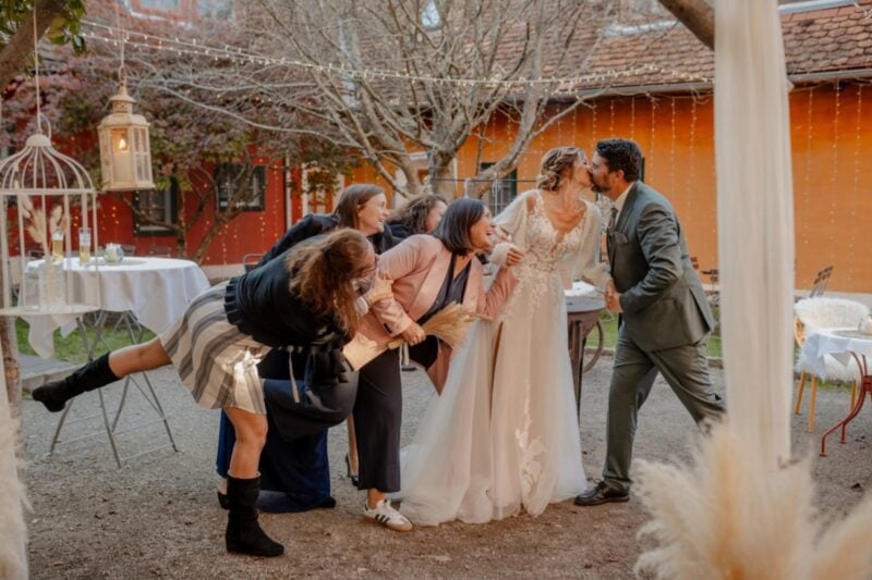 Brautpaar küsst sich im Hof, während Freundinnen die Braut spielerisch zurückhalten