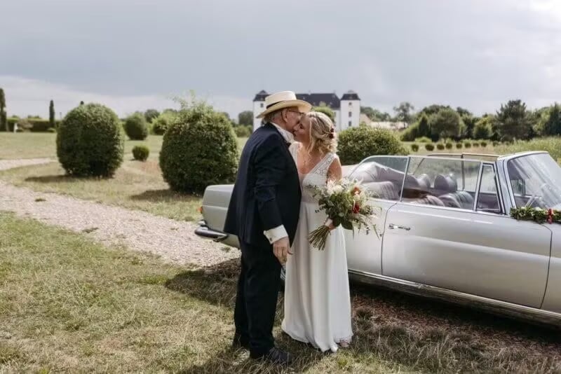 Vater küsst seine Tochter auf die Stirn neben Oldtimer vor Schloss