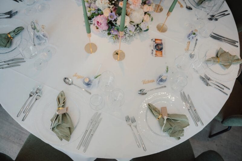Gedeckter Hochzeitstisch mit salbeigrünen Servietten, goldenen Kerzenständern und pastellfarbenem Blumengesteck