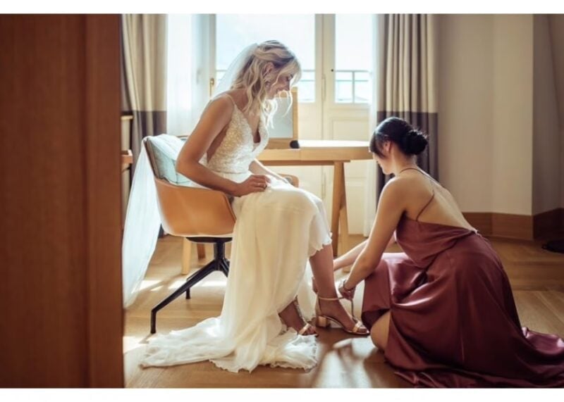 Trauzeugin hilft der Braut beim Anziehen der Schuhe während des Getting Ready