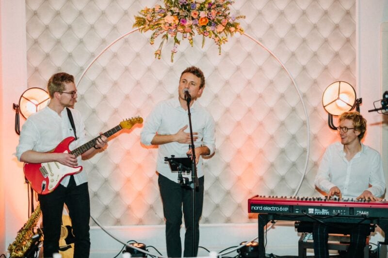 Live-Band mit Sänger, Gitarrist und Keyboarder spielt vor Blumenbogen zur Hochzeitsfeier