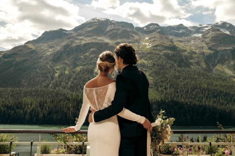 Brautpaar umarmt sich auf Balkon mit Blick auf See und Bergpanorama