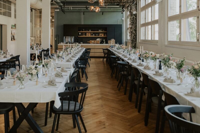 Lange Hochzeitstafel im industriellen Ambiente mit schwarzen Stühlen und pastellfarbener Tischdeko