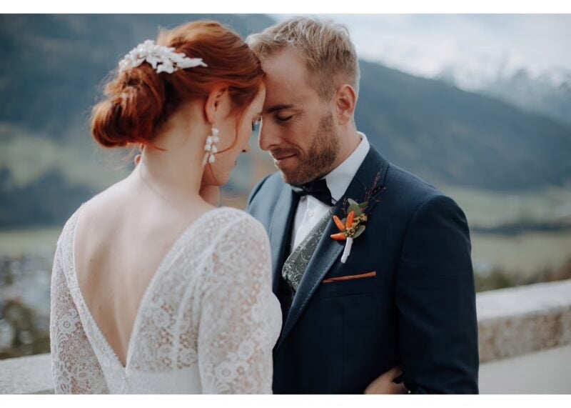 Brautpaar mit Stirn an Stirn, Braut mit Spitzenkleid und Haarschmuck vor Bergpanorama