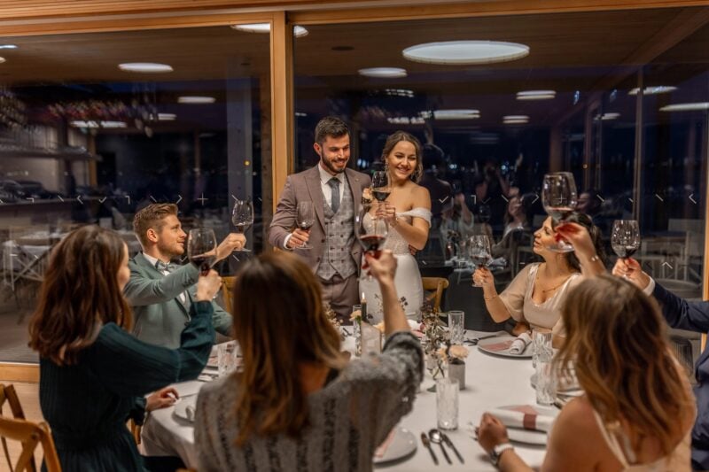 Brautpaar stößt mit Rotwein bei der Hochzeitsfeier am See mit Gästen an