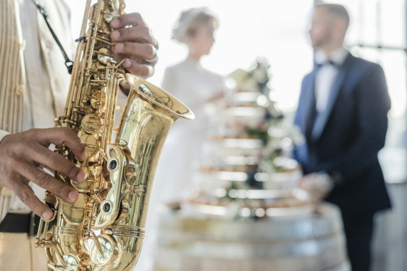 Saxophonist spielt im Vordergrund, Brautpaar mit Hochzeitstorte im Hintergrund