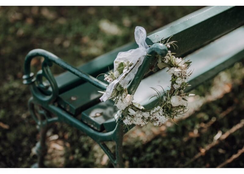 Blumenkranz aus getrockneten weißen Blüten hängt an einer grünen Parkbank