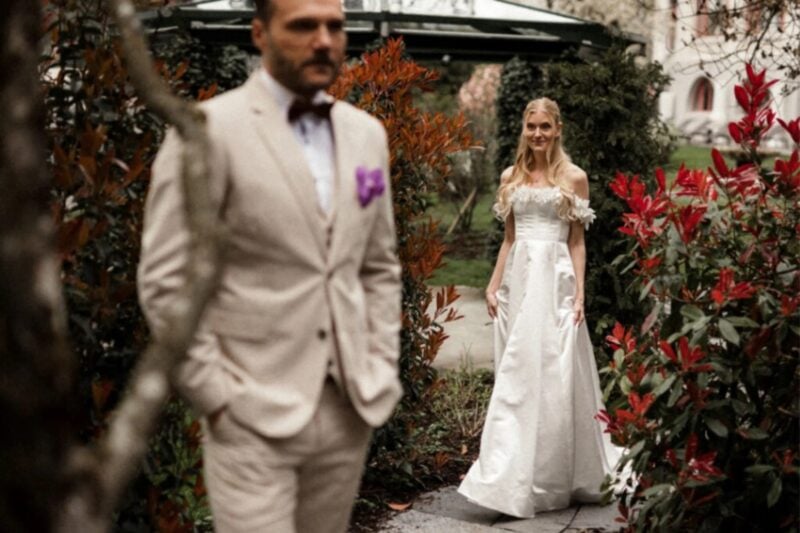 First-Look-Moment: Braut nähert sich Bräutigam im herbstlichen Schlossgarten