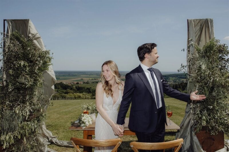 Brautpaar geht Hand in Hand zur Zeremonie mit Panoramablick – wann humorvolle Glückwünsche gut passen