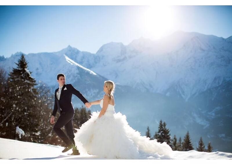 Brautpaar spaziert Hand in Hand durch den Schnee vor verschneiten Alpengipfeln beim Chalet d'Adrien
