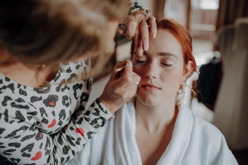 Make-up-Artistin trägt einer rothaarigen Braut im Hotel Schloss Mittersill Eyeliner auf