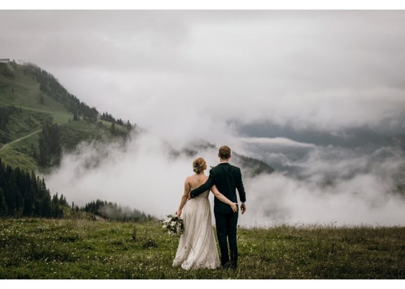 Brautpaar spaziert Hand in Hand durch eine nebelverhangene Alpenlandschaft