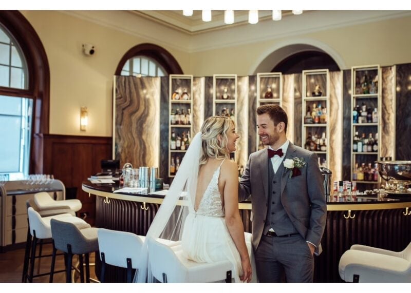 Brautpaar lehnt lächelnd an der eleganten Hotelbar des Kempinski Palace Engelberg – stilvolles Hochzeitsfoto