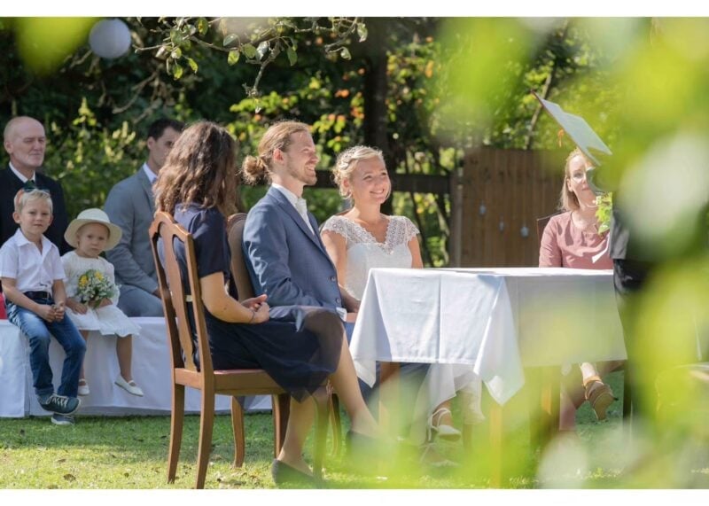 Brautpaar sitzt bei der freien Trauung im Garten von Schlossgut Gundersdorf, umgeben von Trauzeugen und Hochzeitsgästen