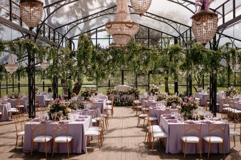 Wedding breakfast room decorated with chandeliers, greenery and lilac linens