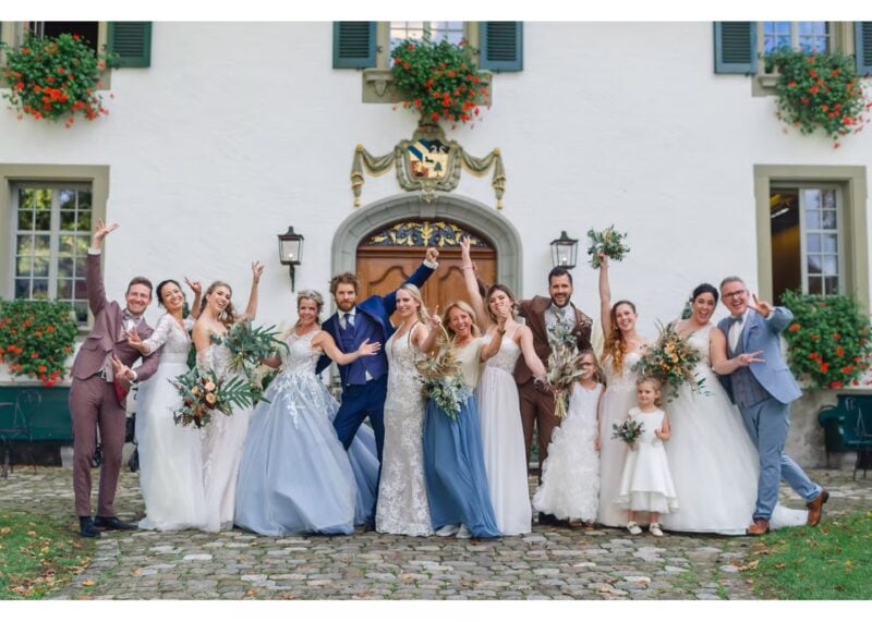 Brautpaar und Hochzeitsgesellschaft posieren ausgelassen vor dem Schloss