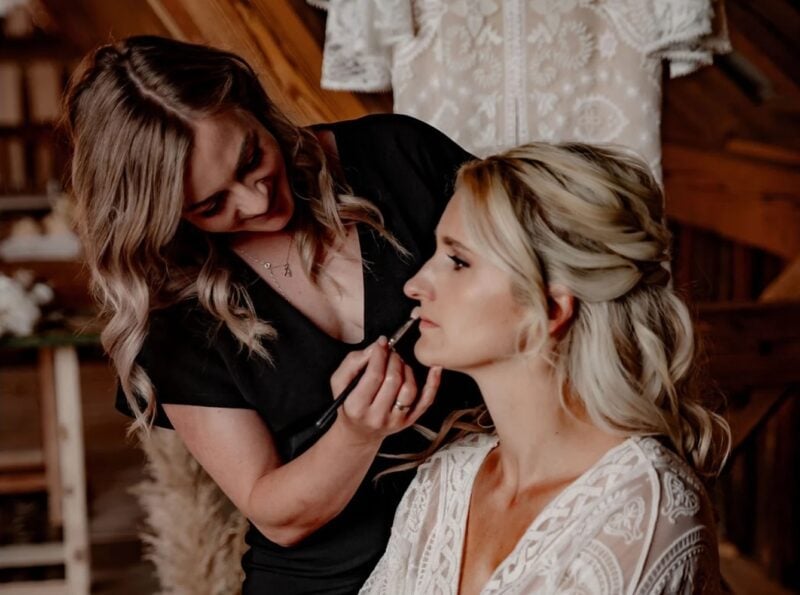 Make-up-Artistin schminkt die Lippen einer Braut im rustikalen Ambiente