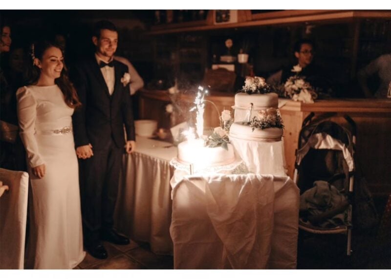 Brautpaar steht neben der Hochzeitstorte mit Wunderkerze – krönender Abschluss der Hochzeitsunterhaltung