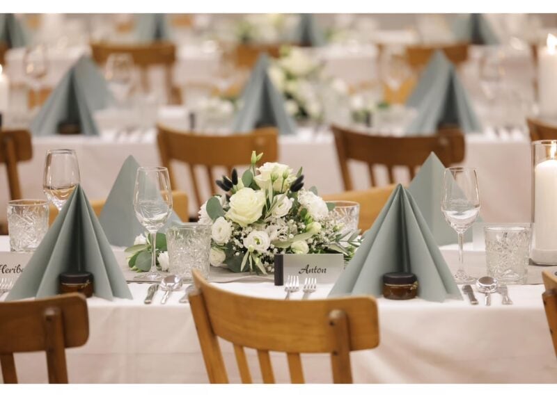 Gedeckter Hochzeitstisch mit Namenskärtchen, salbeigrünen Servietten und weißem Blumengesteck im Weinhof & Feiergut F. Kohl