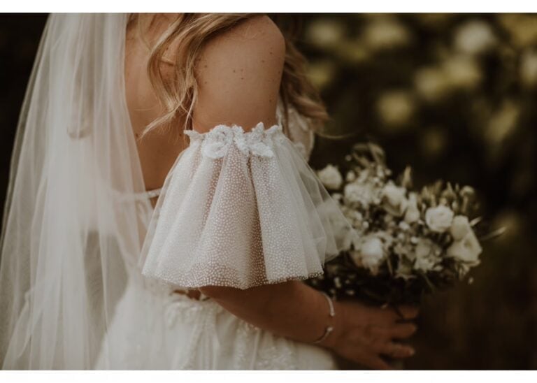 Detailaufnahme von Brautkleid-Ärmel aus Tüll mit weißem Brautstrauß aus Rosen