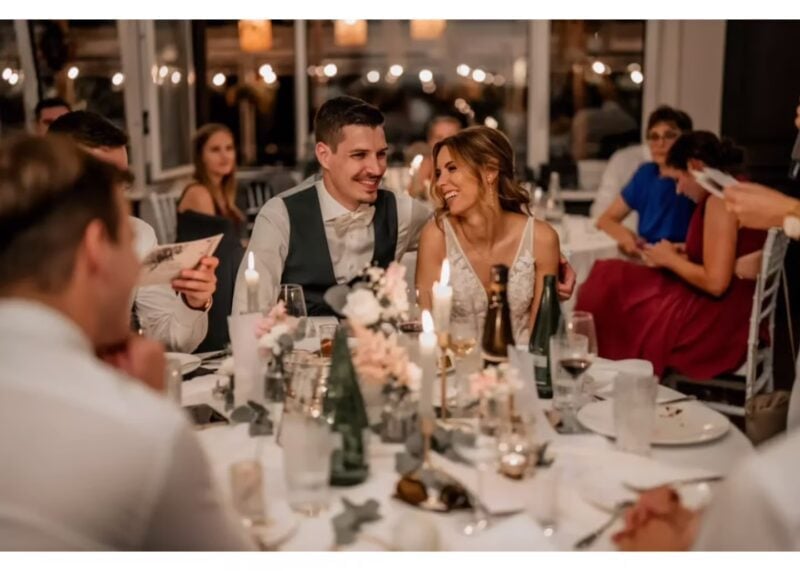 Brautpaar liest lachend Glückwunschkarten an der festlich gedeckten Hochzeitstafel im Hotel Uto Kulm
