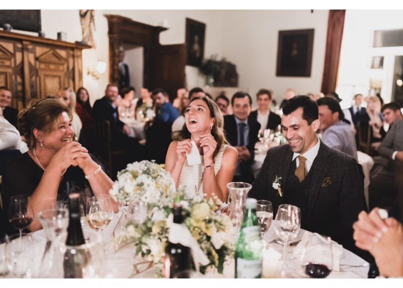 Lachende Hochzeitsgäste und Brautpaar an einer festlich gedeckten runden Tafel im Schloss Ernegg