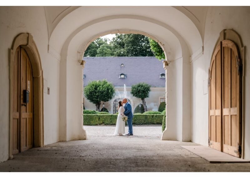 Brautpaar küsst sich im Innenhof von Schloss Halbturn, eingerahmt von einem hellen Torbogen