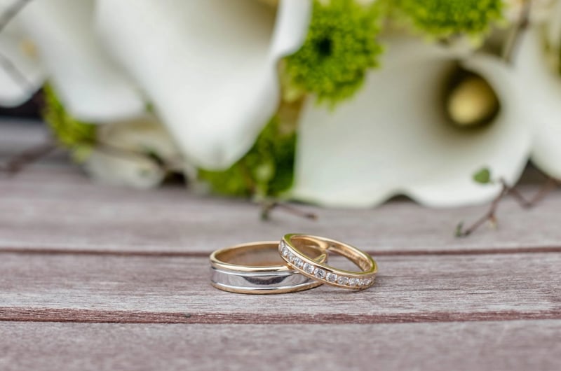 A pair of wedding rings on a table with flowers in the background