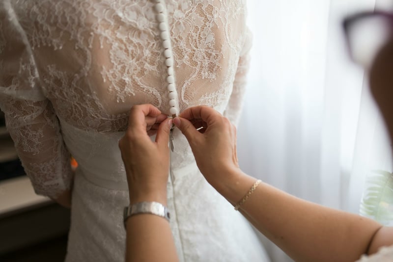 Maid of honour helping fasten the brides dress