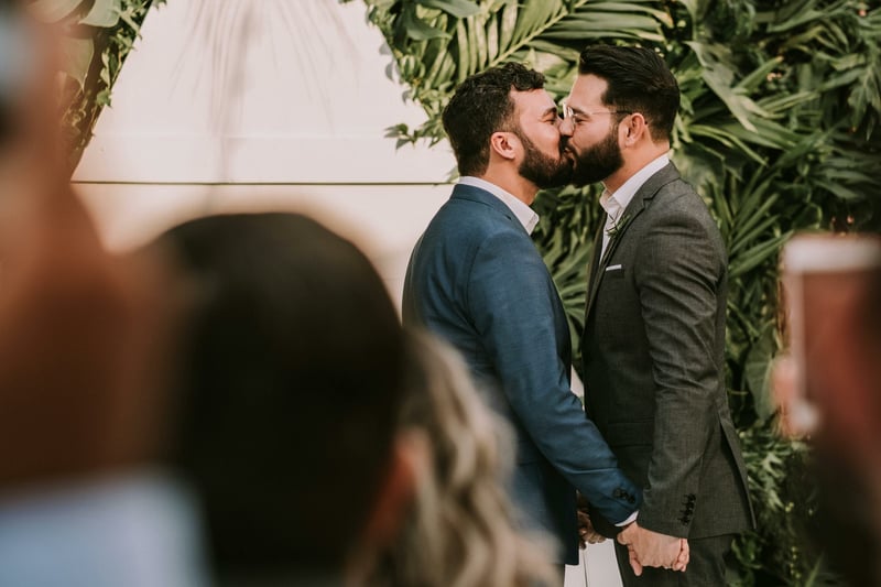 Two grooms kissing during an outdoor wedding ceremony