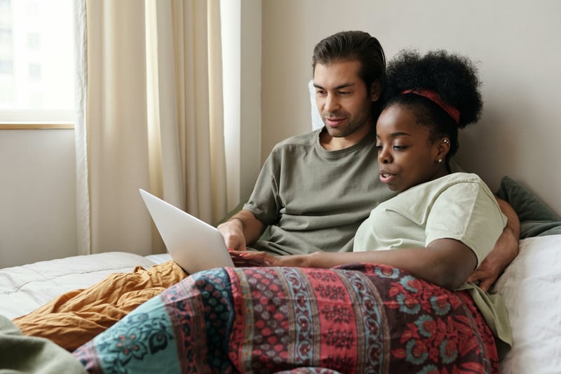 Couple lying in bed working on their wedding website together