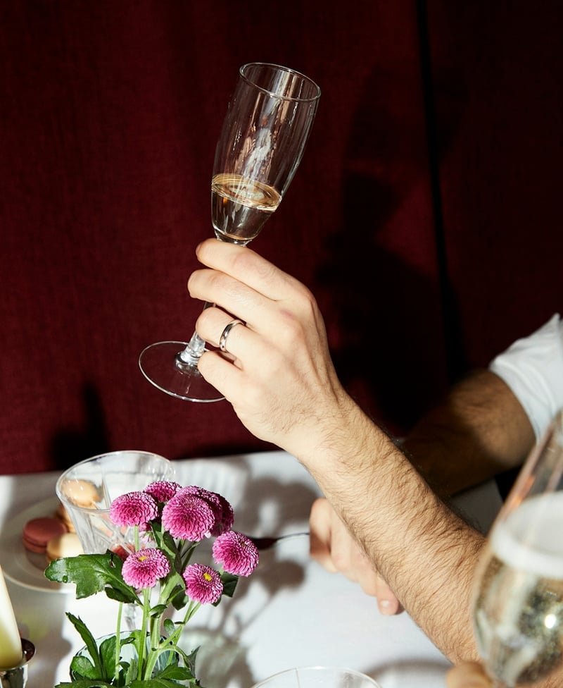 man's hand holding a glass of champagne showing off a silver wedding ring
